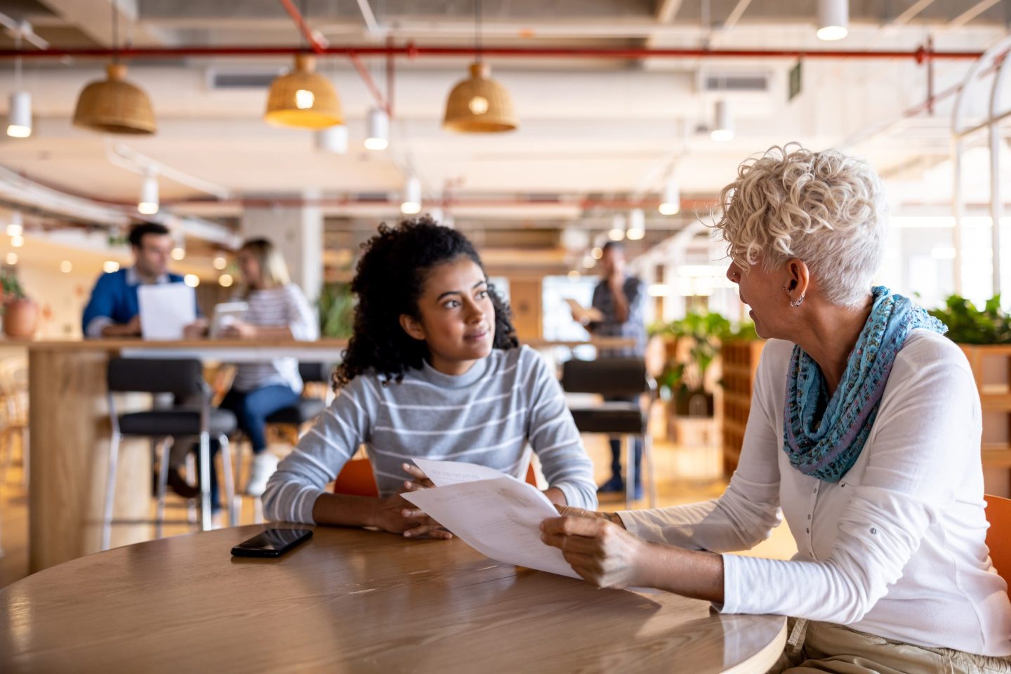Latin American businesswoman interviewing a young woman for a job at a coworking and holding her CV - employment concepts