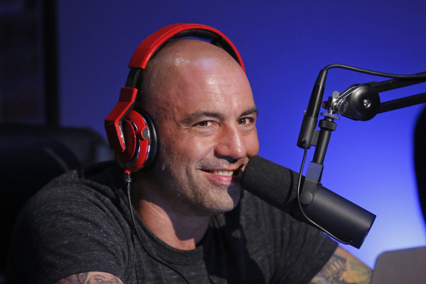 Joe Rogan wears red headphones and smiles.