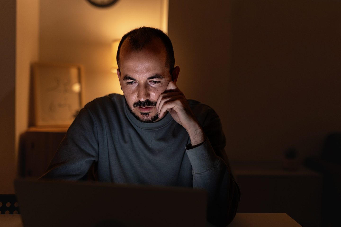 Young man looking worriedly at his laptop screen while working from home at night. People and home office concept.