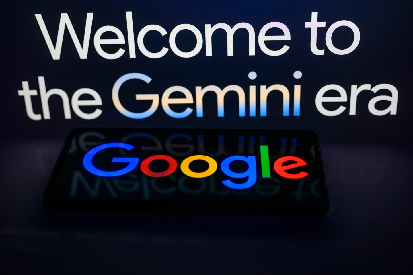 A smart phone displaying Google with the Gemini web page slogan in the background is featured in this photo illustration