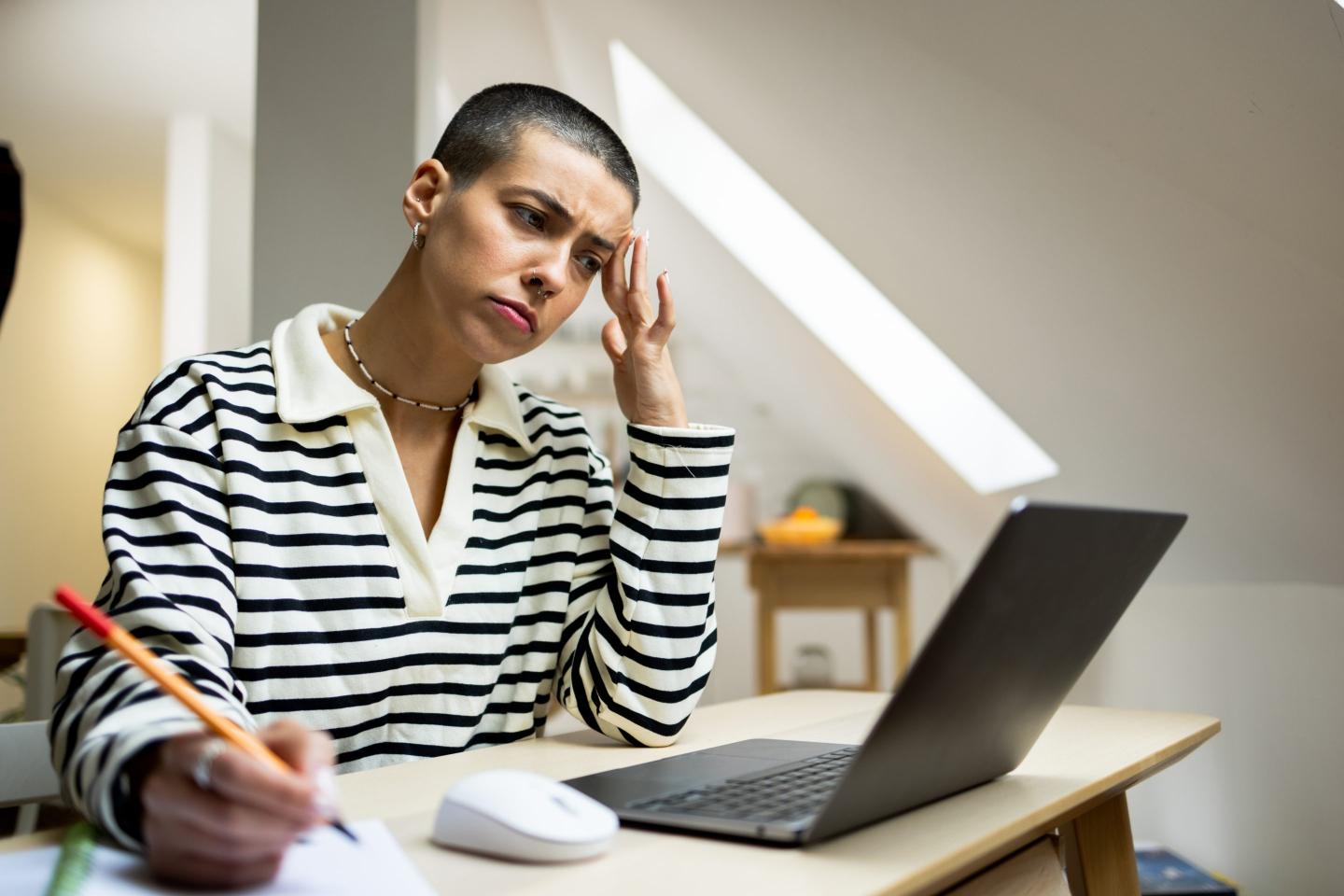 person at their desk with a laptop in front of them looking worried