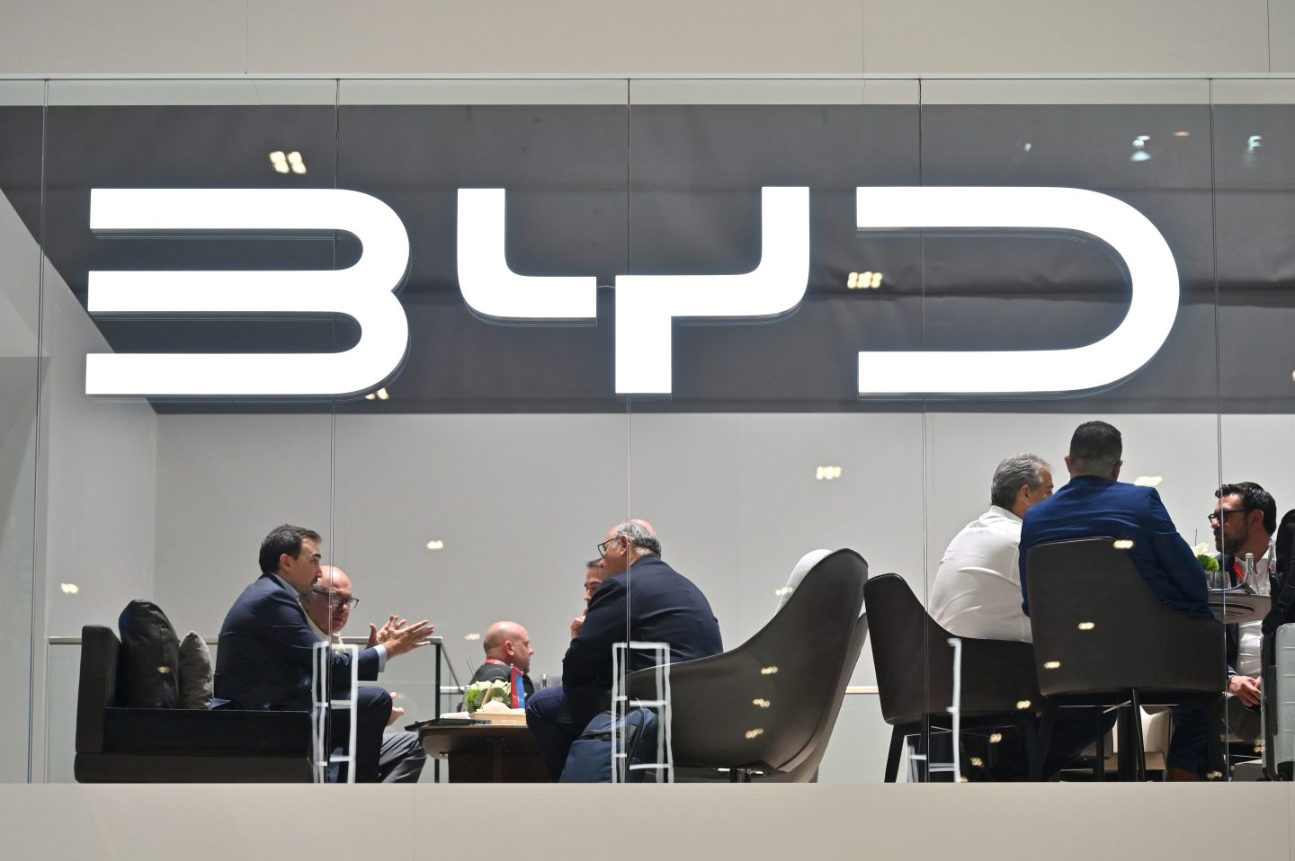 People do business behind a BYD logo at the Geneva International Motor Show on Feb. 26, 2024.