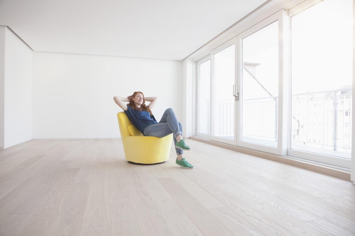 Woman lounging in yellow chair in empty apartment