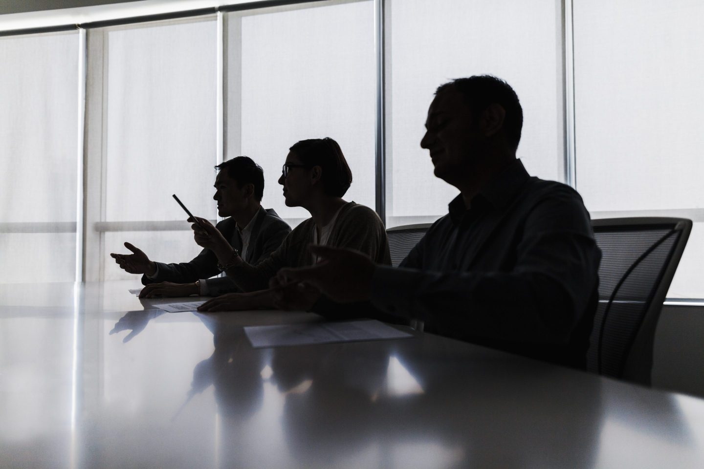Silhouette of three business people sitting at meeting table.