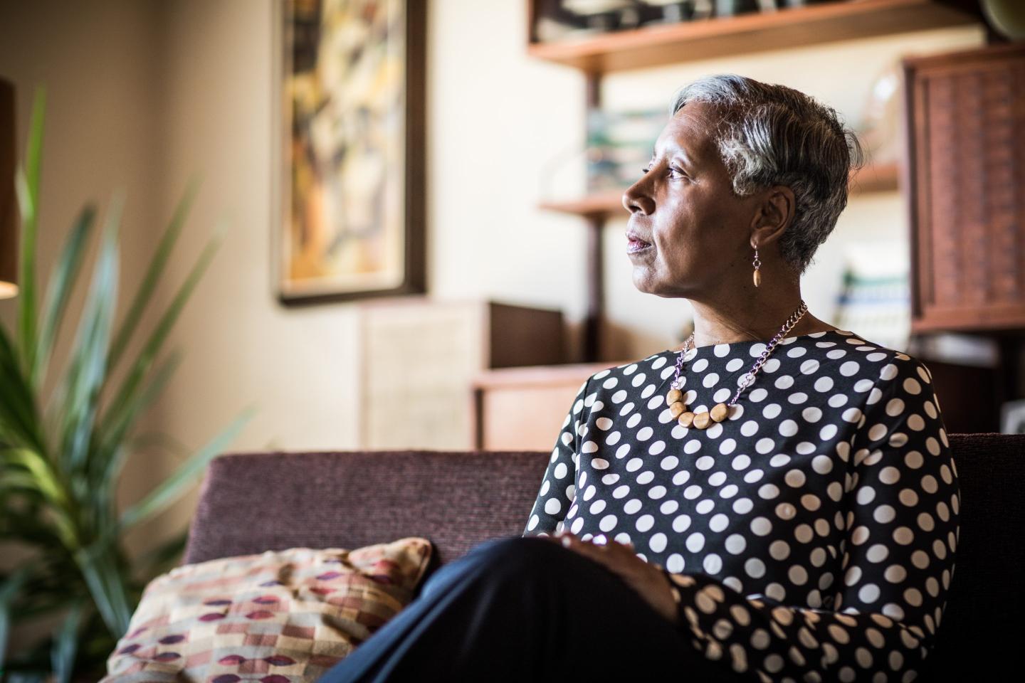 Photo of a woman looking pensive, sitting on a couch at home