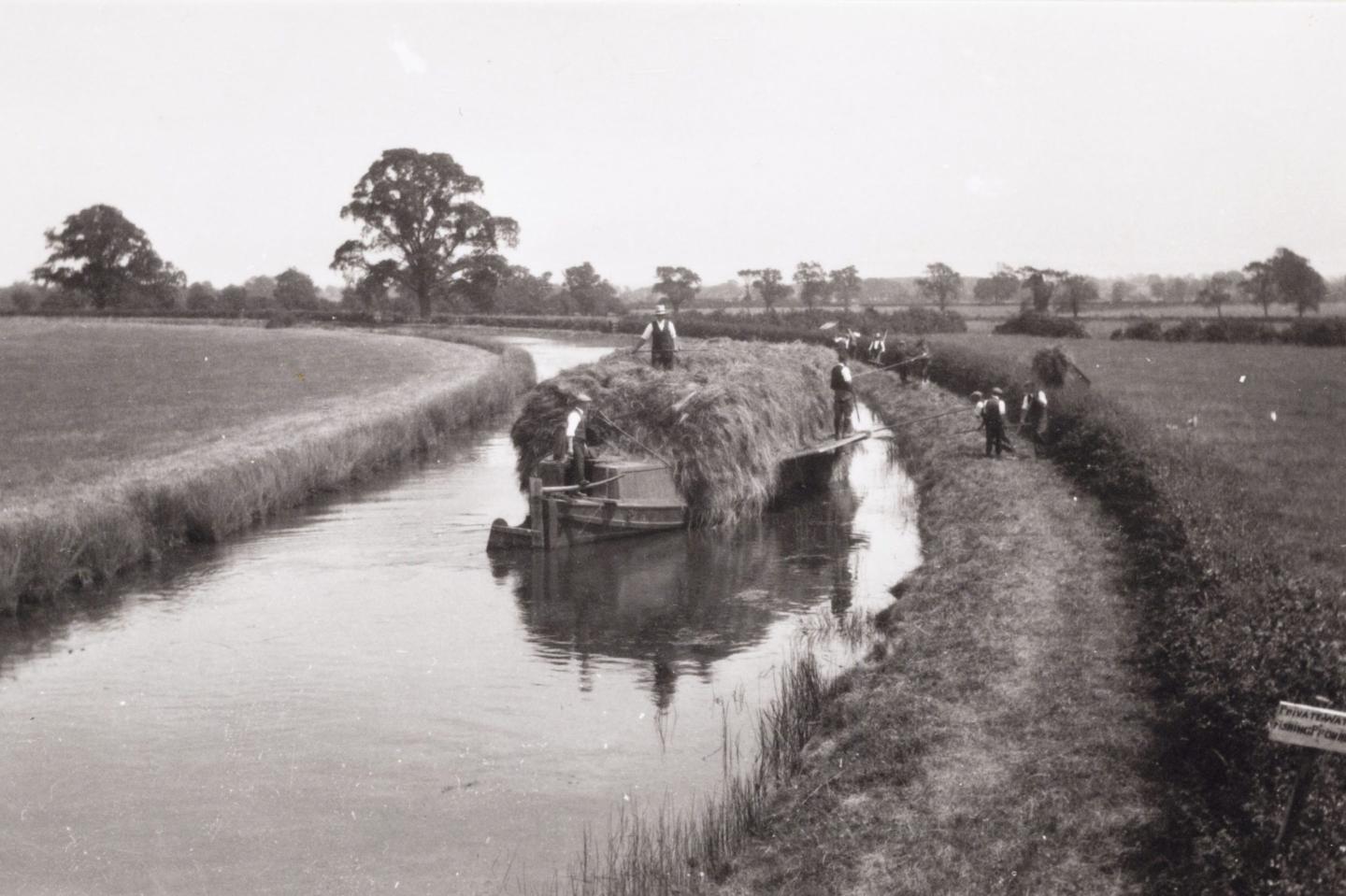 Black and white photo of a hay bale on a boat on a canal