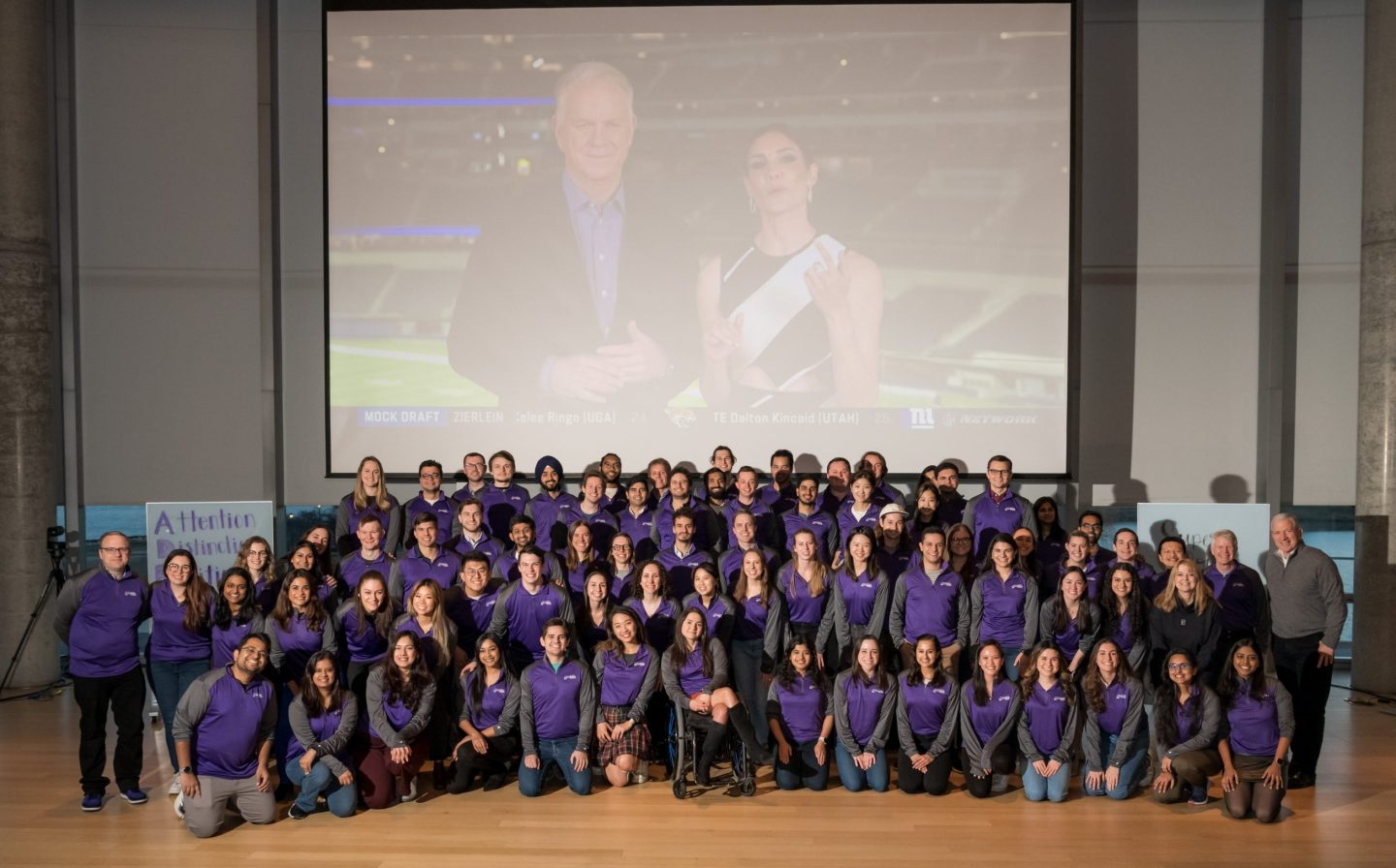 Several dozen participants of Kellogg School of Management's 2023 ad review pose for a group photograph in front of a projector screen.