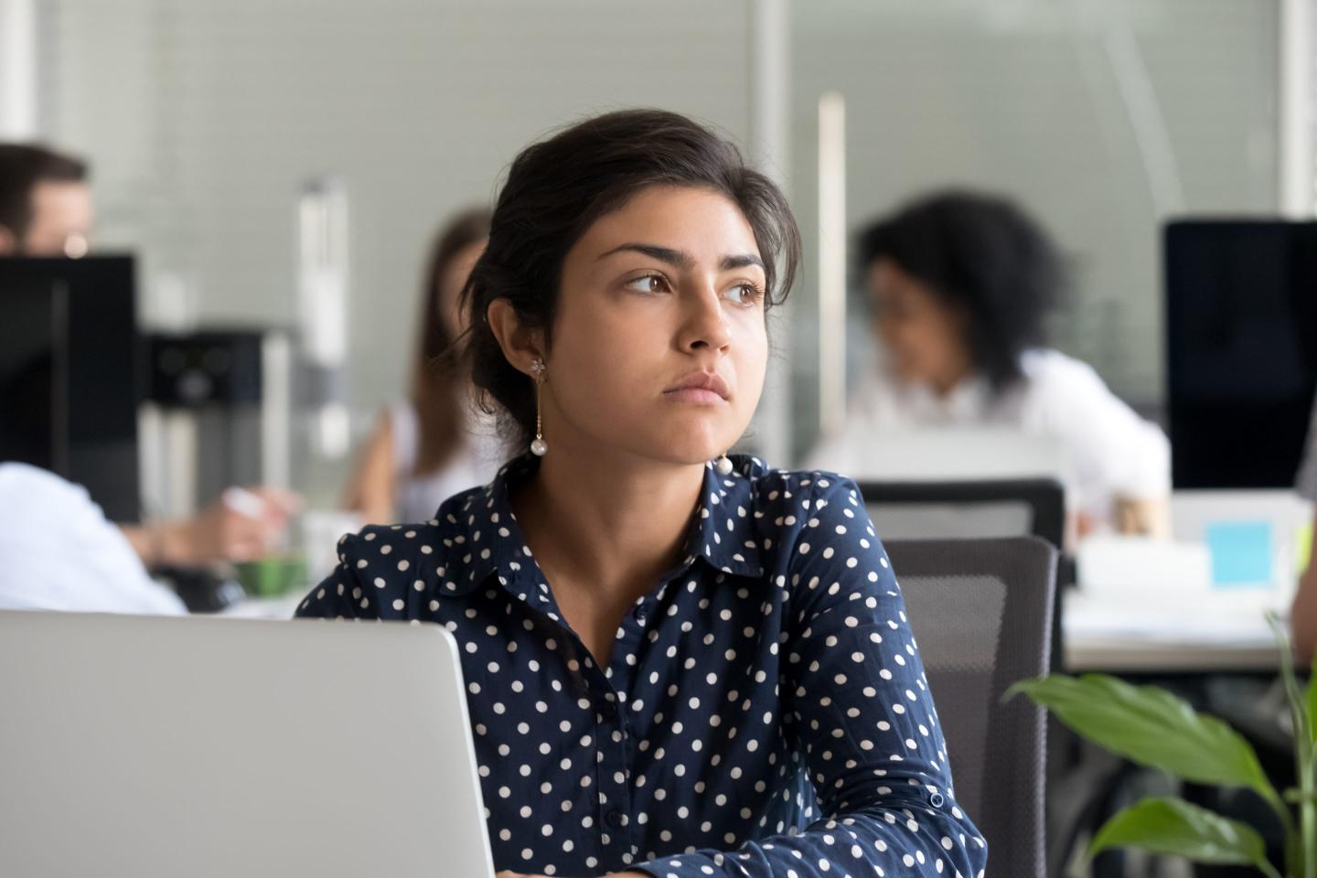 Photo of young woman at work looking away from her computer screen