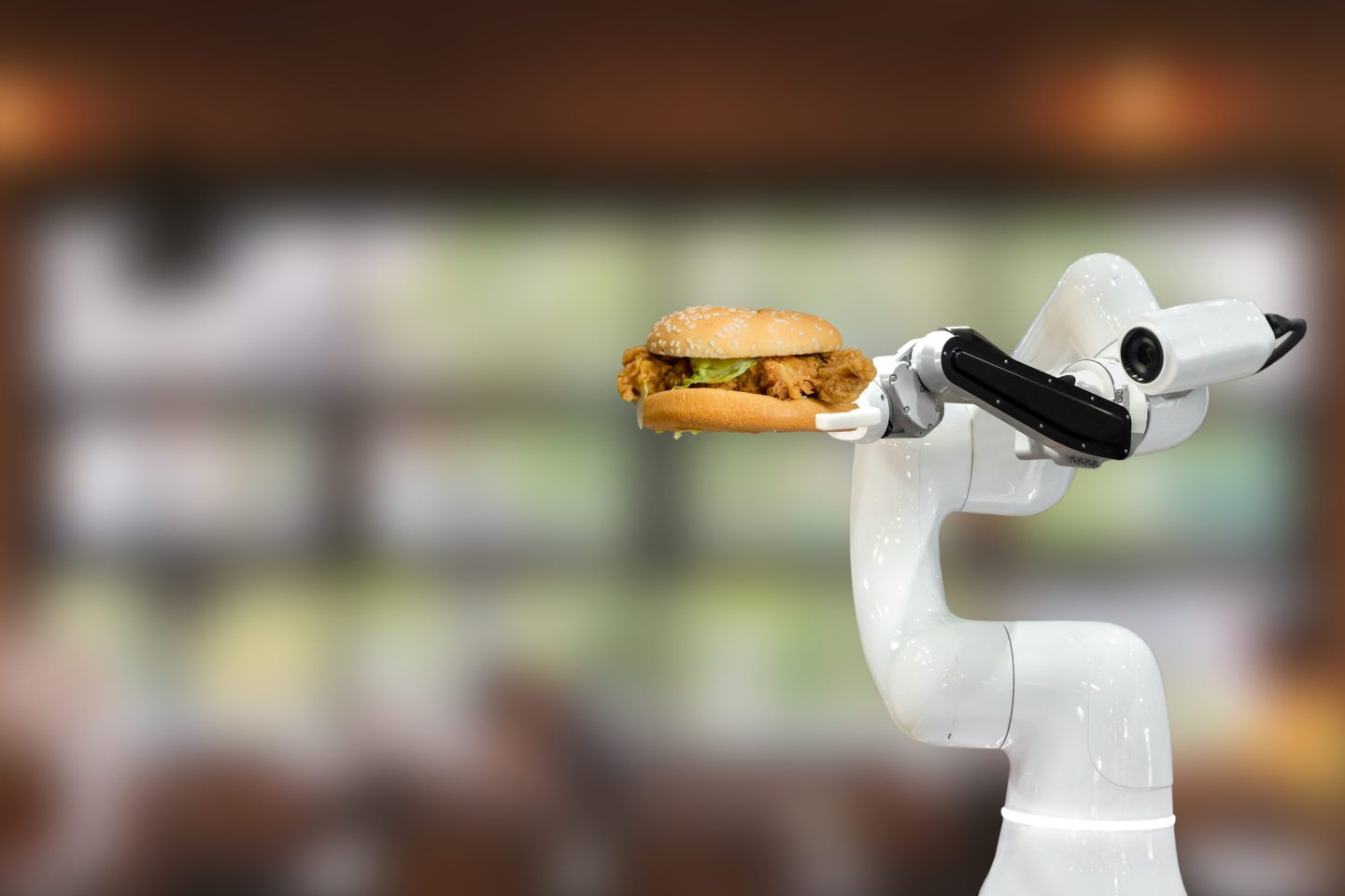A robot arm lifts up a chicken sandwich.
