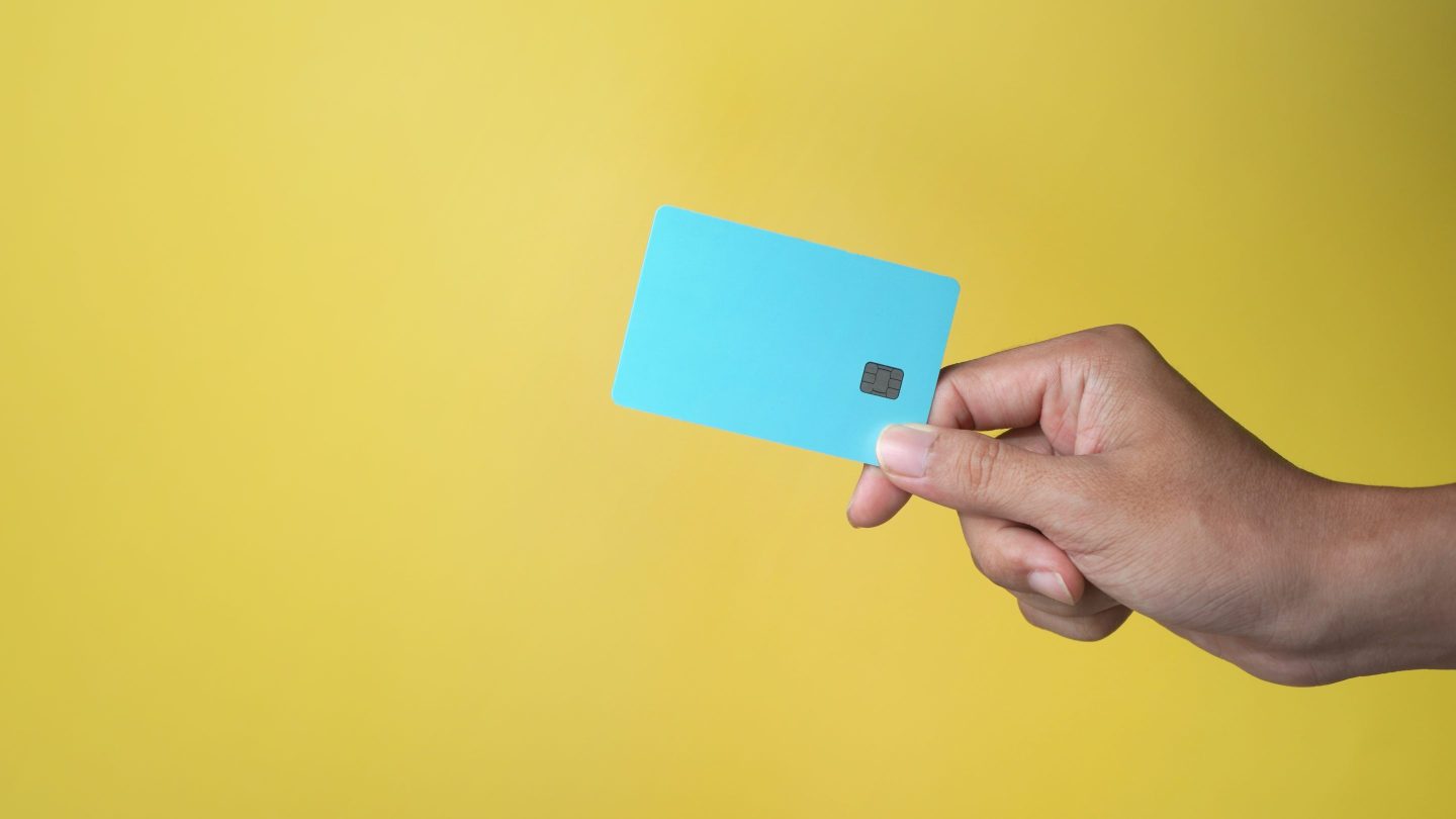 hand holding blue credit card with yellow background and copy space