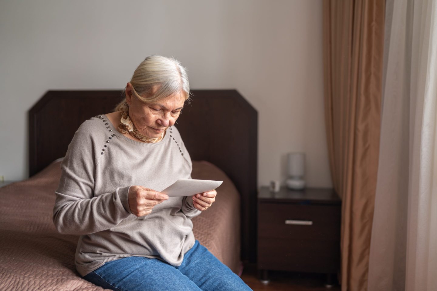 A senior sits on a bed, looking at a photo
