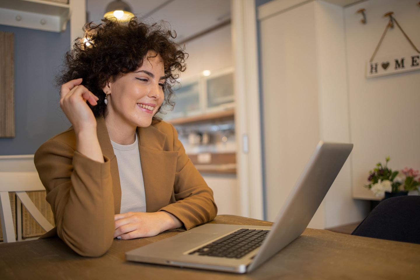 A young woman wearing business casual attire attends a virtual meeting from her home.