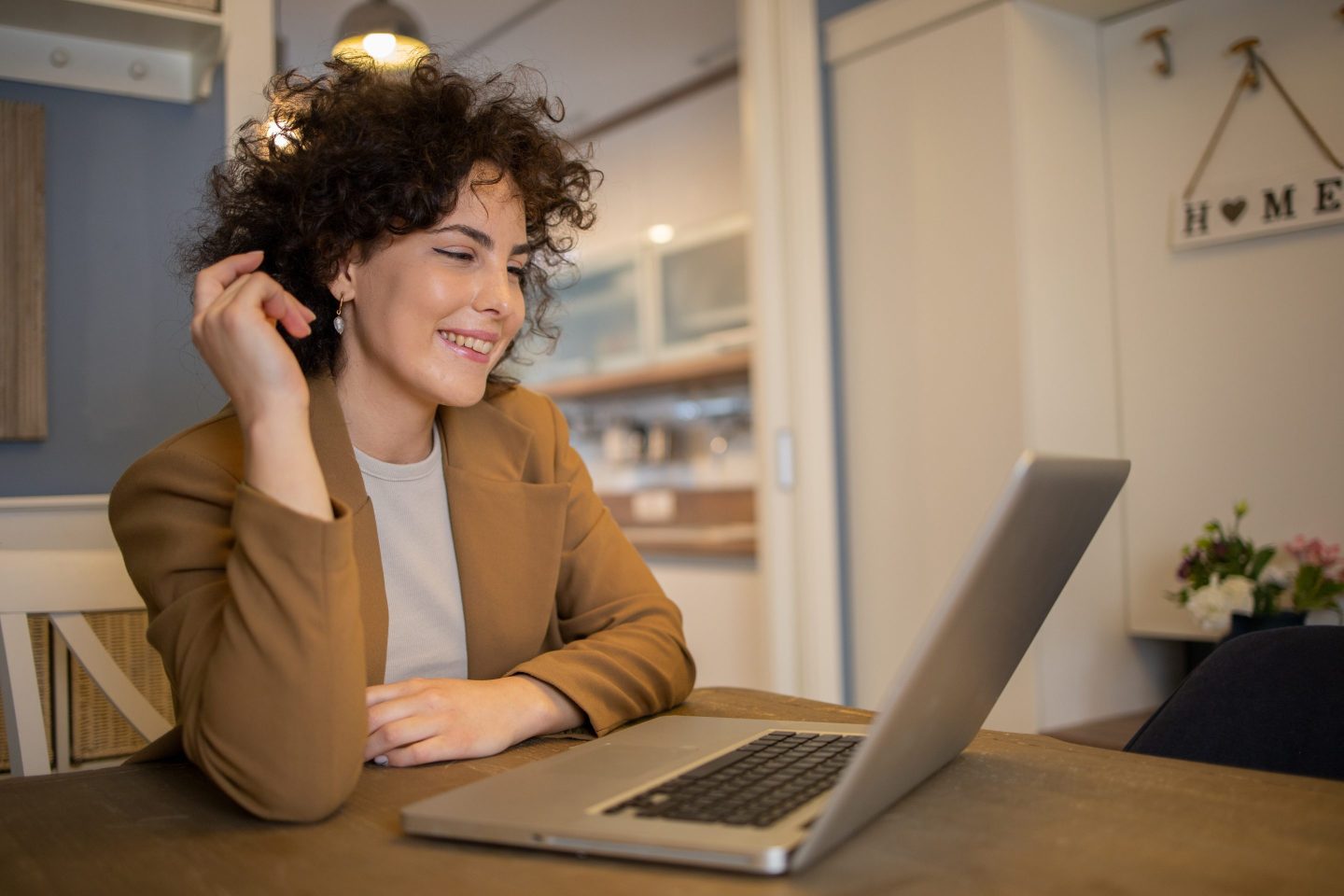 A young woman wearing business casual attire attends a virtual meeting from her home.