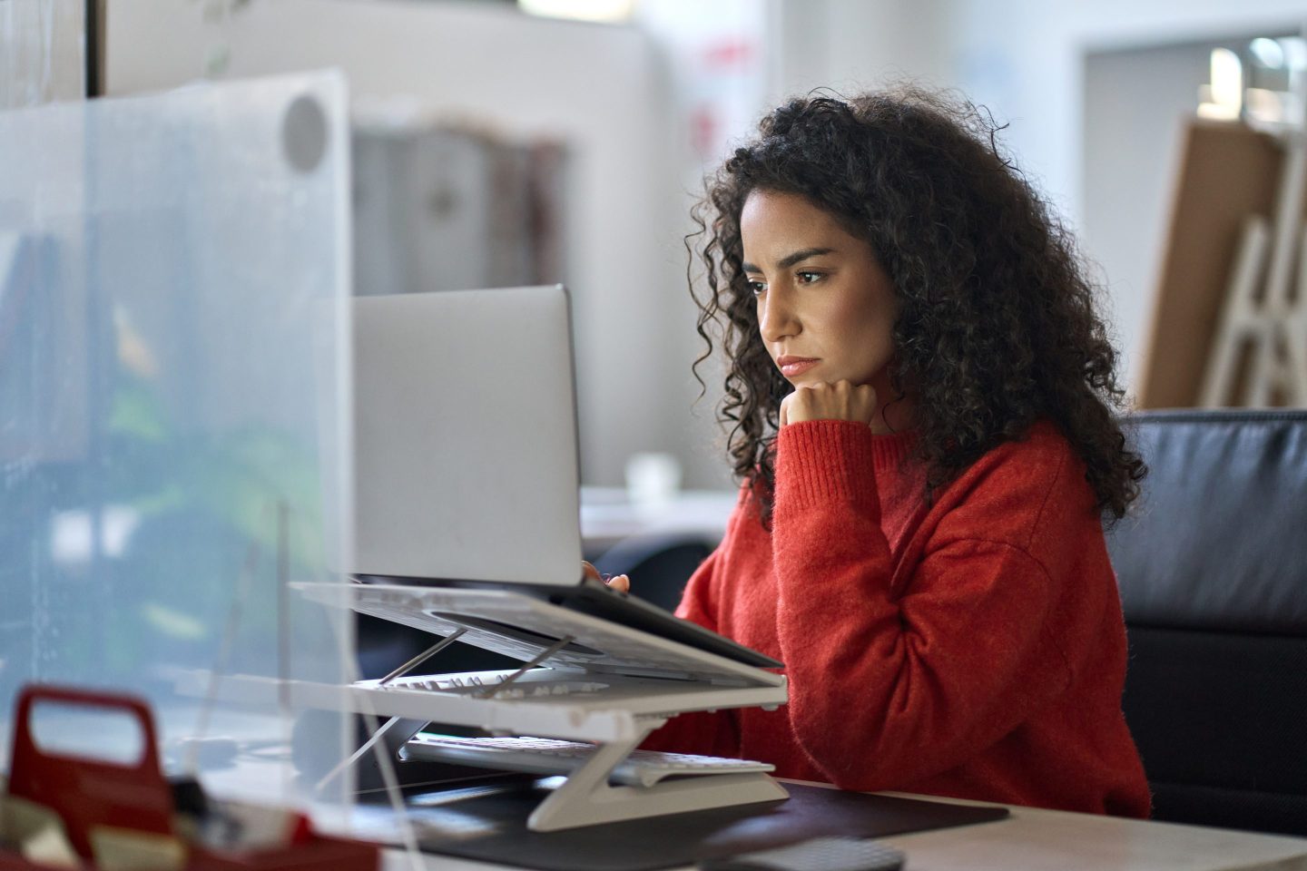 A young woman is working from a laptop in an office setting.