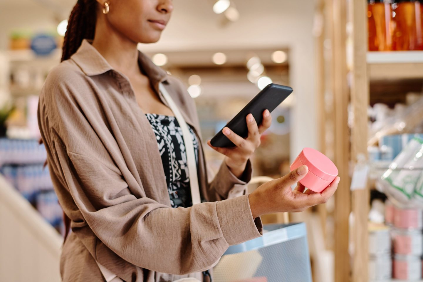 Shopper looks at phone while holding a tub of face cream