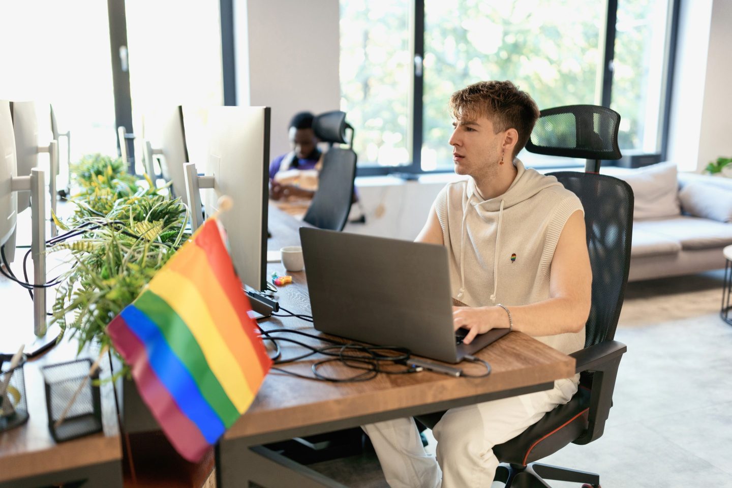 A young man works at a desk in an office. A pride flag is displayed on the desk.