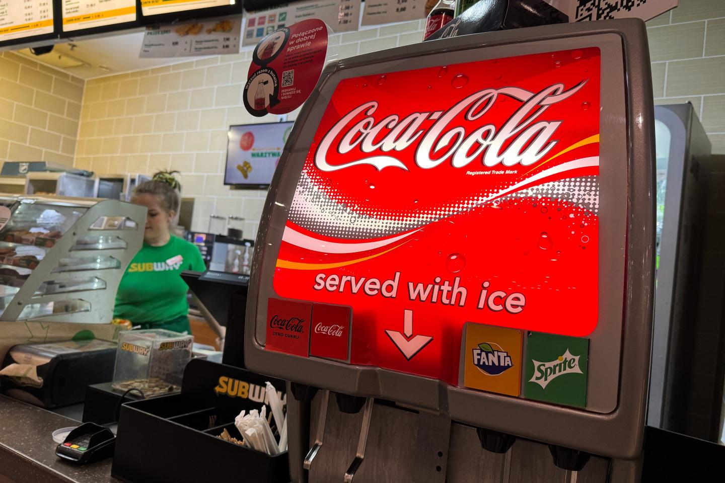 A Coca-Cola soda dispenser next to a Subway cashier