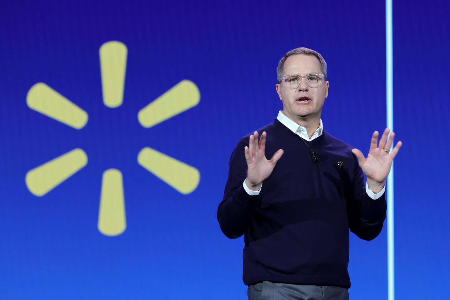 Walmart CEO Doug McMillion is standing in front of a big blue screen with the Walmart logo on it.