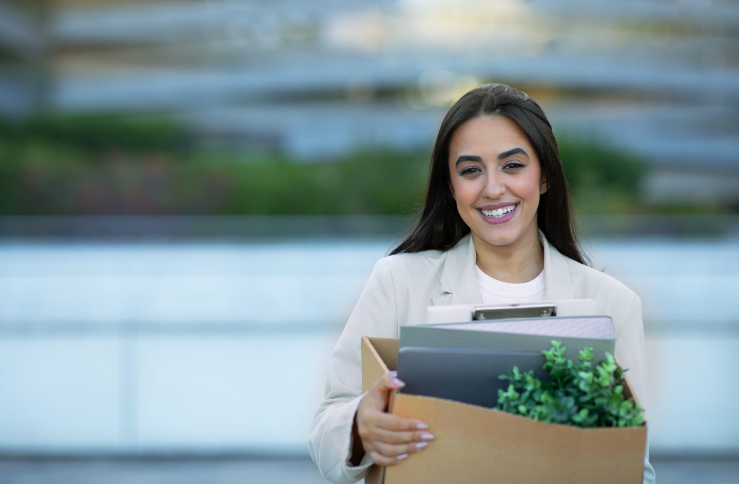 Cheerful businesswoman with box of belongings standing near office building