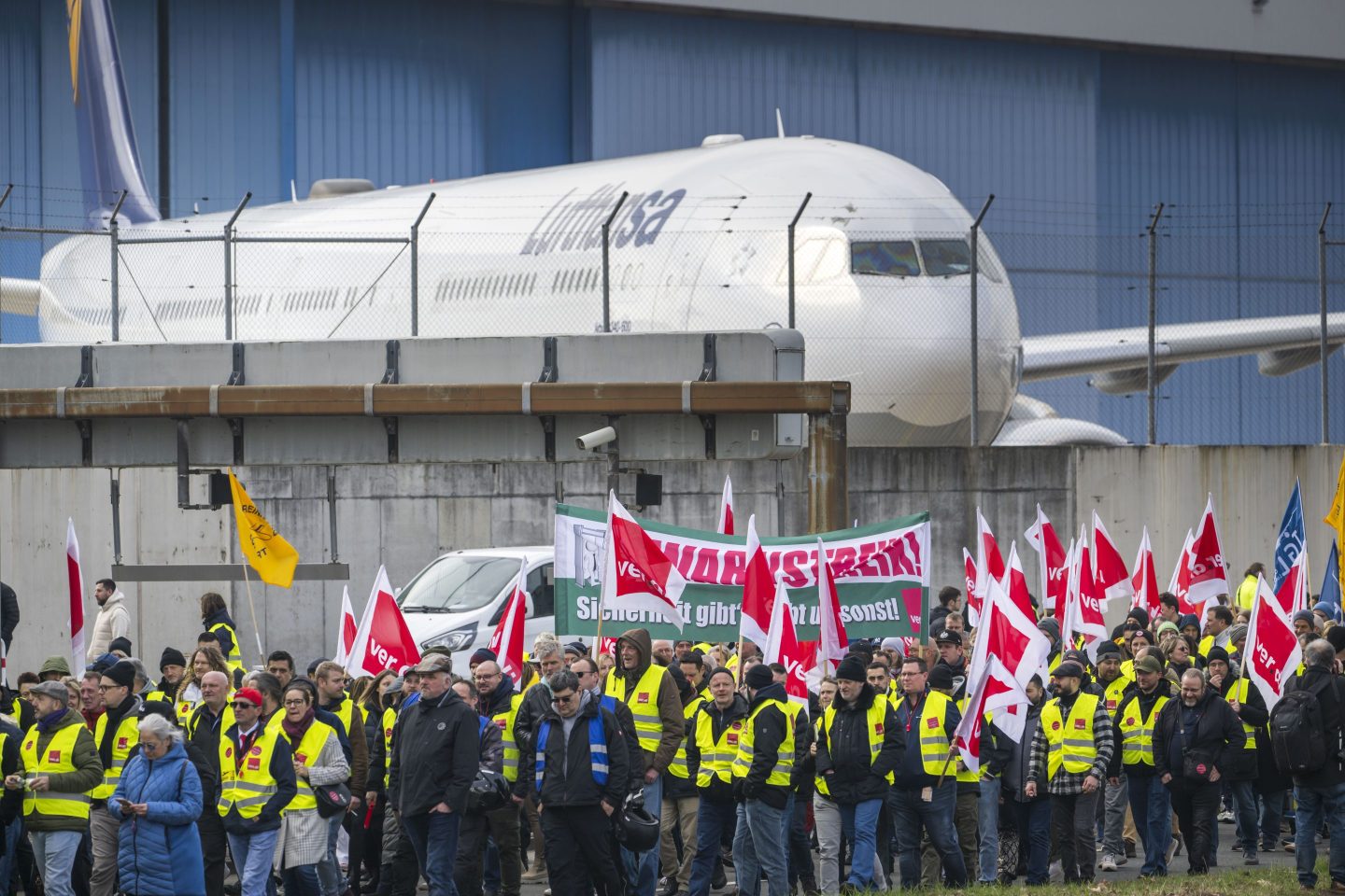 A group of people working for Lufthansa standing holding red flags in protest of Lufthansa