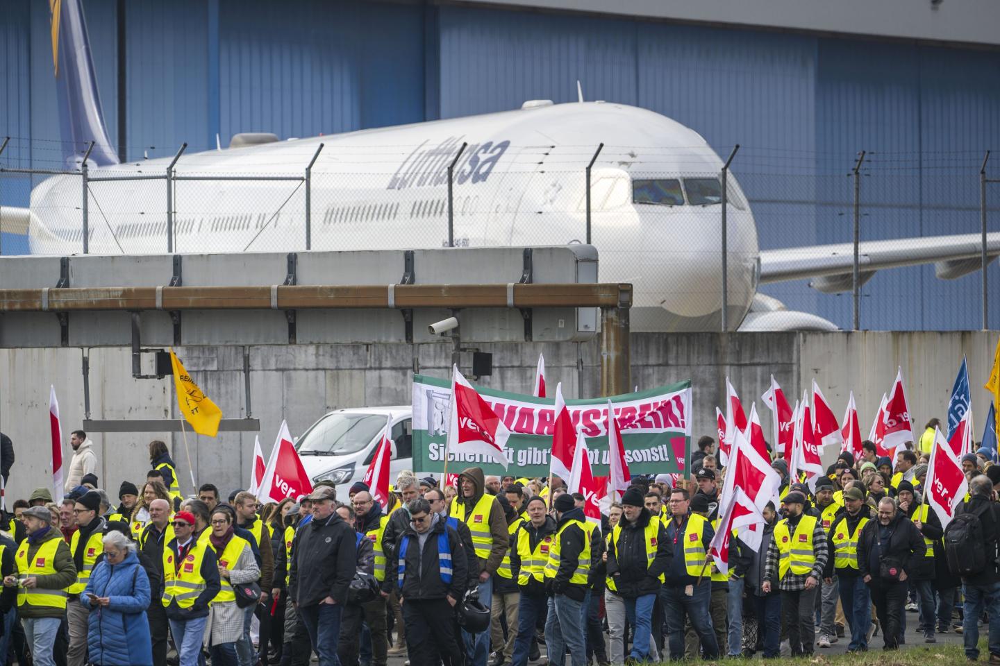 A group of people working for Lufthansa standing holding red flags in protest of Lufthansa