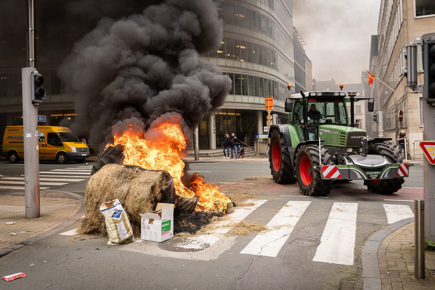 a tractor on a road crossing with a pile of items on fire on the left