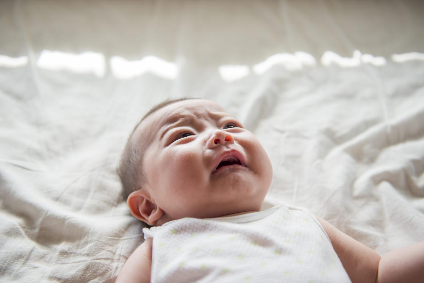 A baby is lying on a white sheet and is crying.