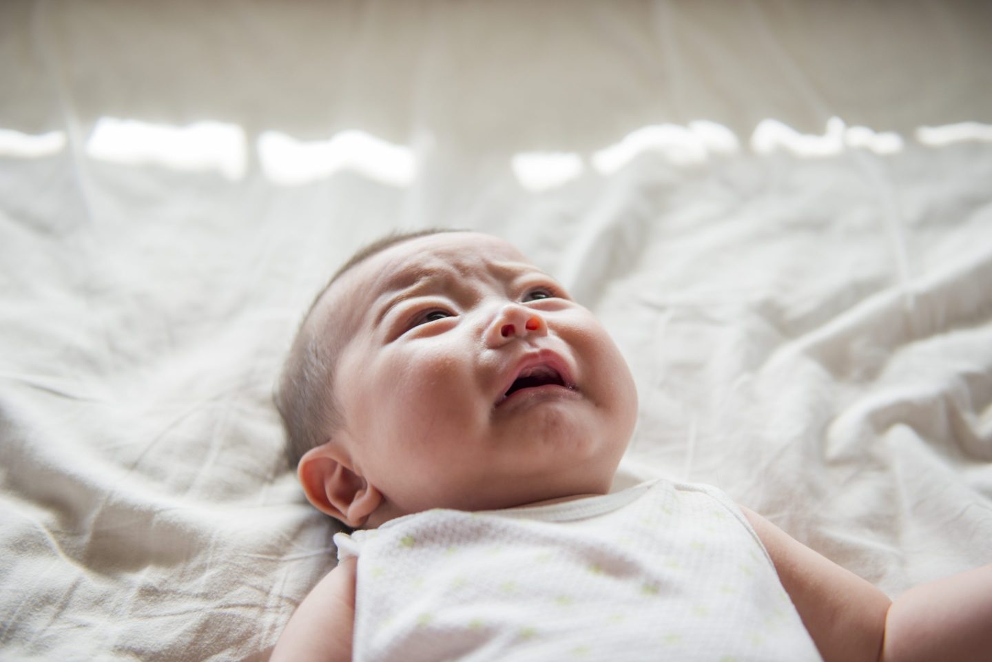A baby is lying on a white sheet and is crying.