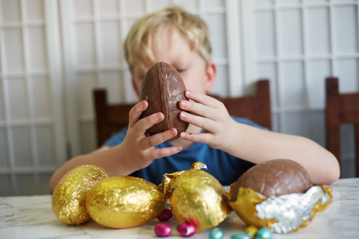 boy seen sitting on a table with golden wrapped chocolate eggs