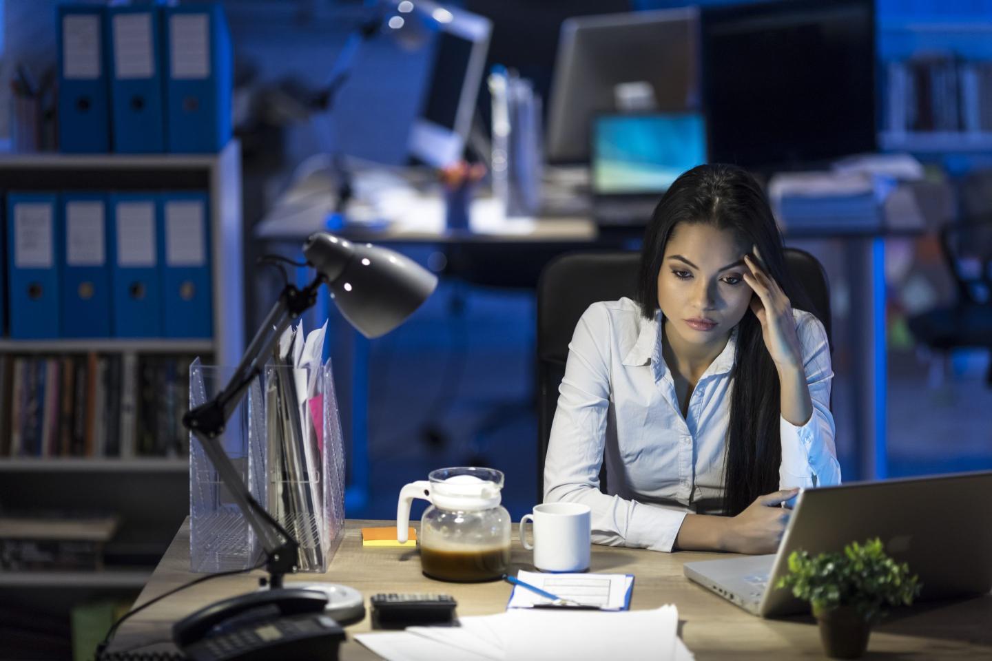 Employee sits at her desk, stressed with work.