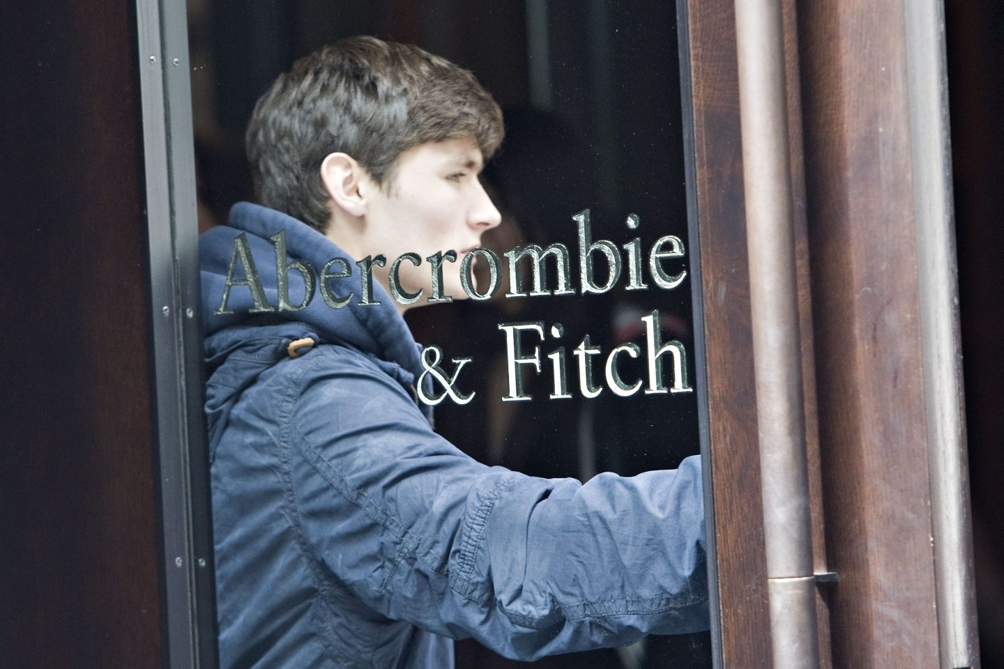 A man with a navy jacket stands in the window of a store with "Abercrombie & Fitch" embossed on it.