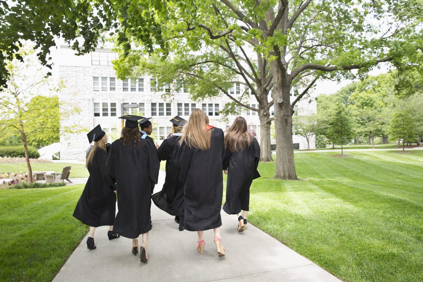 Back view of students in black graduation gowns. Four out of the six are also wearing the cap.