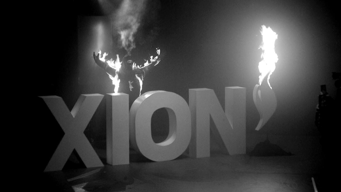 Person in costume standing behind a logo of XION, which is on fire