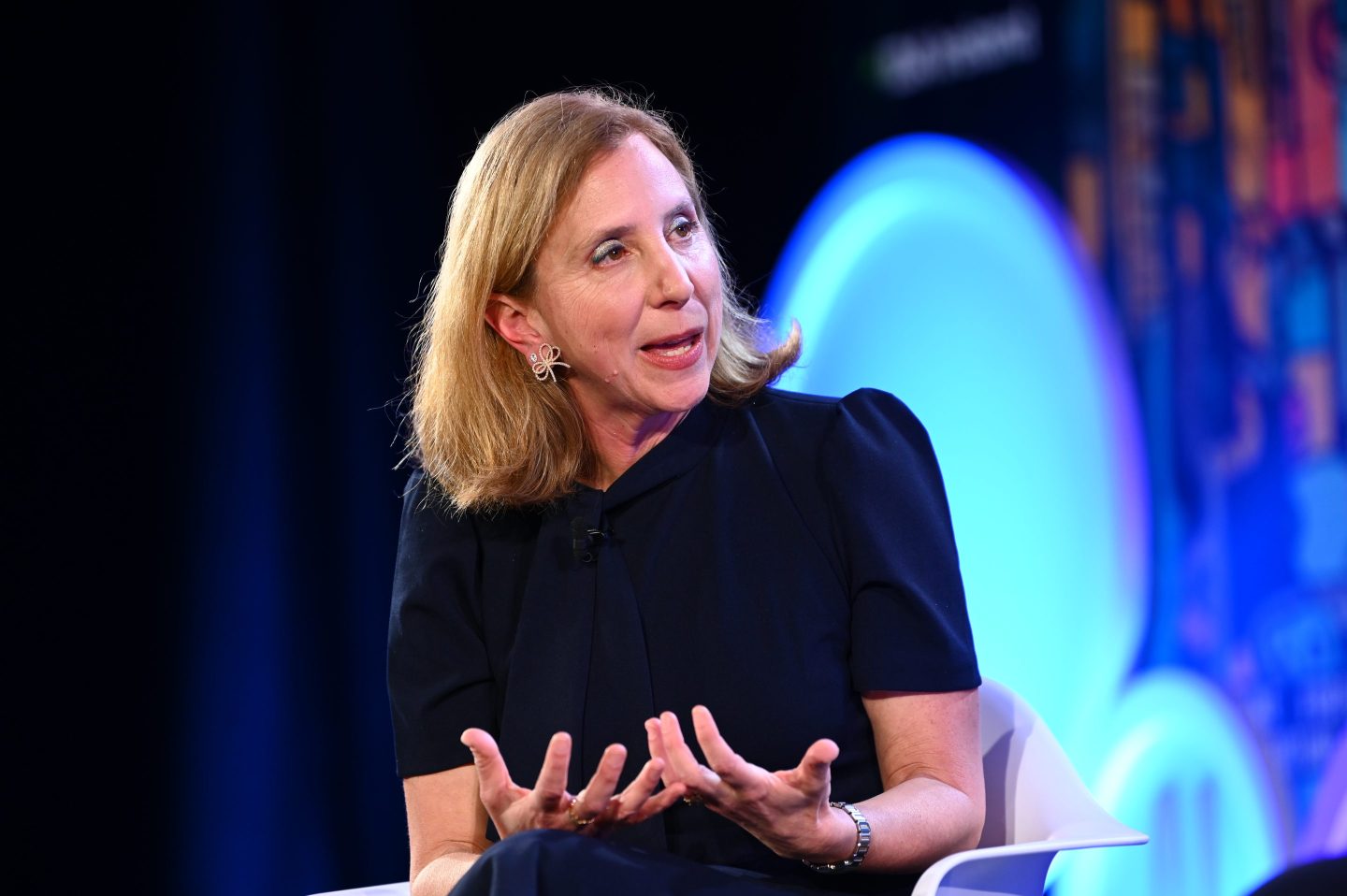 Paula Goldman is sitting in front of a bright blue background gesturing while she speaks.