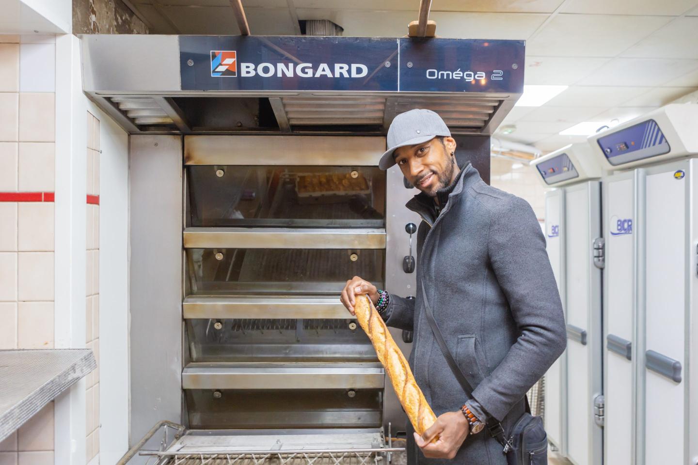 Xavier Netry stands in front of a bread oven holding a baguette.