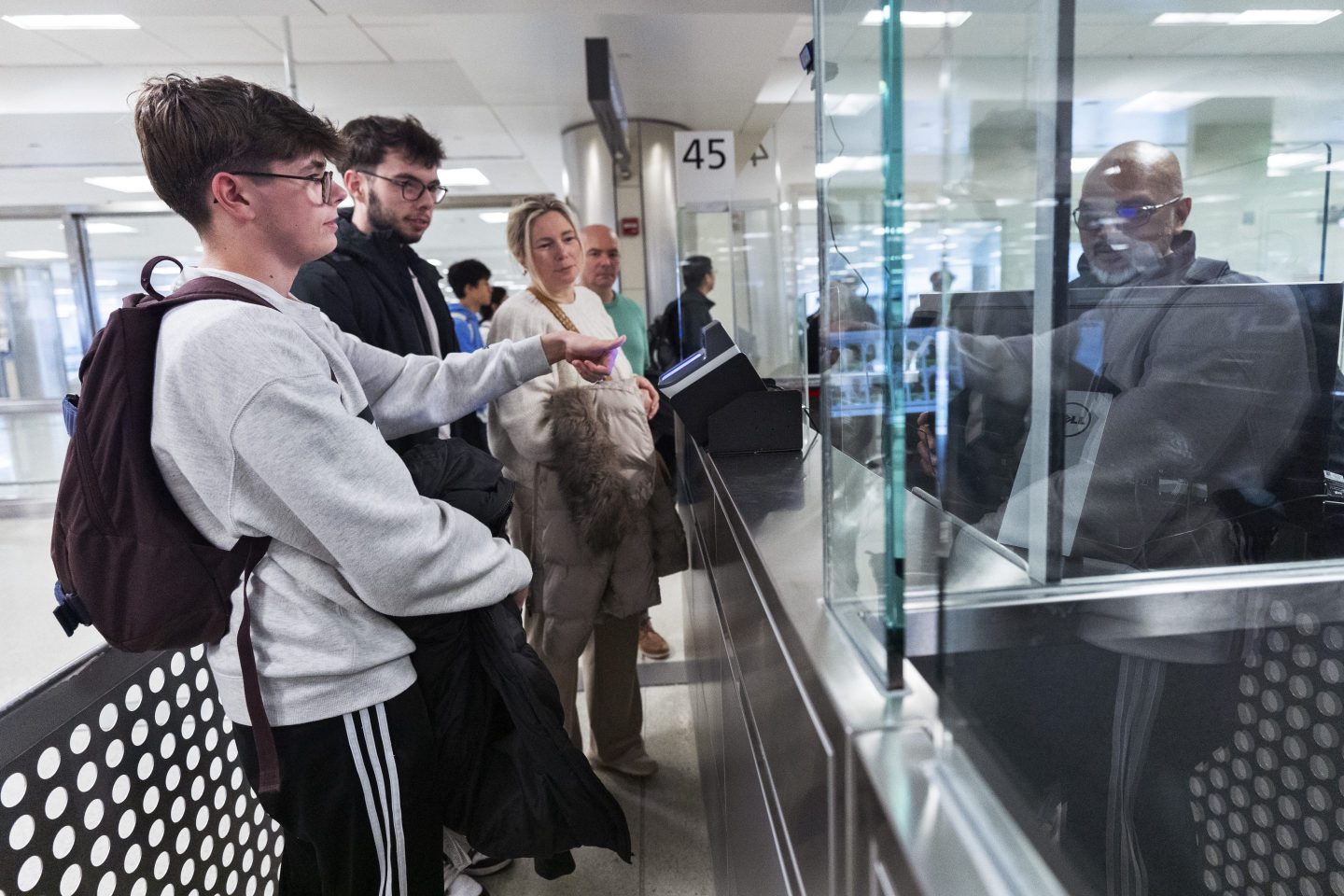 Piet De Staercke, from back right to left, with his wife Jill Bornauw, their eldest son Stan De Staercke, watch their youngest Tuur de Staercke, get screened by a Custom Border Protection officer, right, in the port of entry at Washington Dulles International Airport in Chantilly, Va. on April 1, 2024.