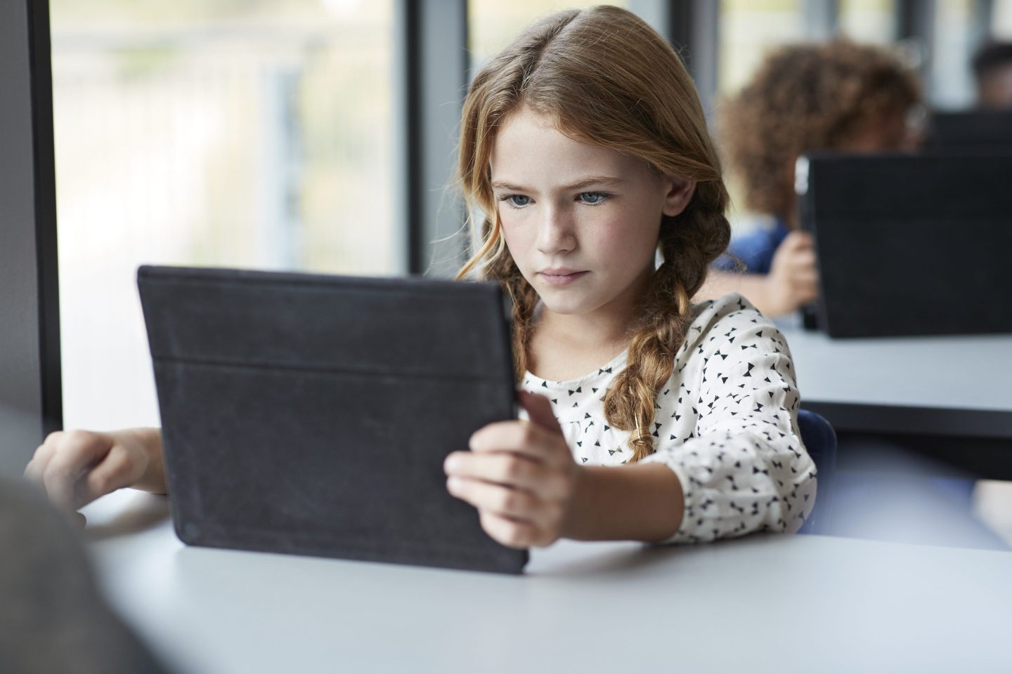 A girl is sitting at a table and looking at an iPad.