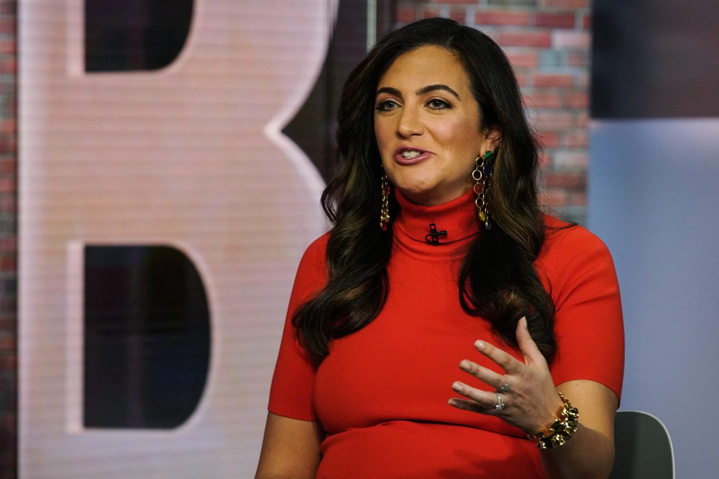 Rent the Runway CEO Jennifer Hyman is wearing a red dress and gesturing while speaking.