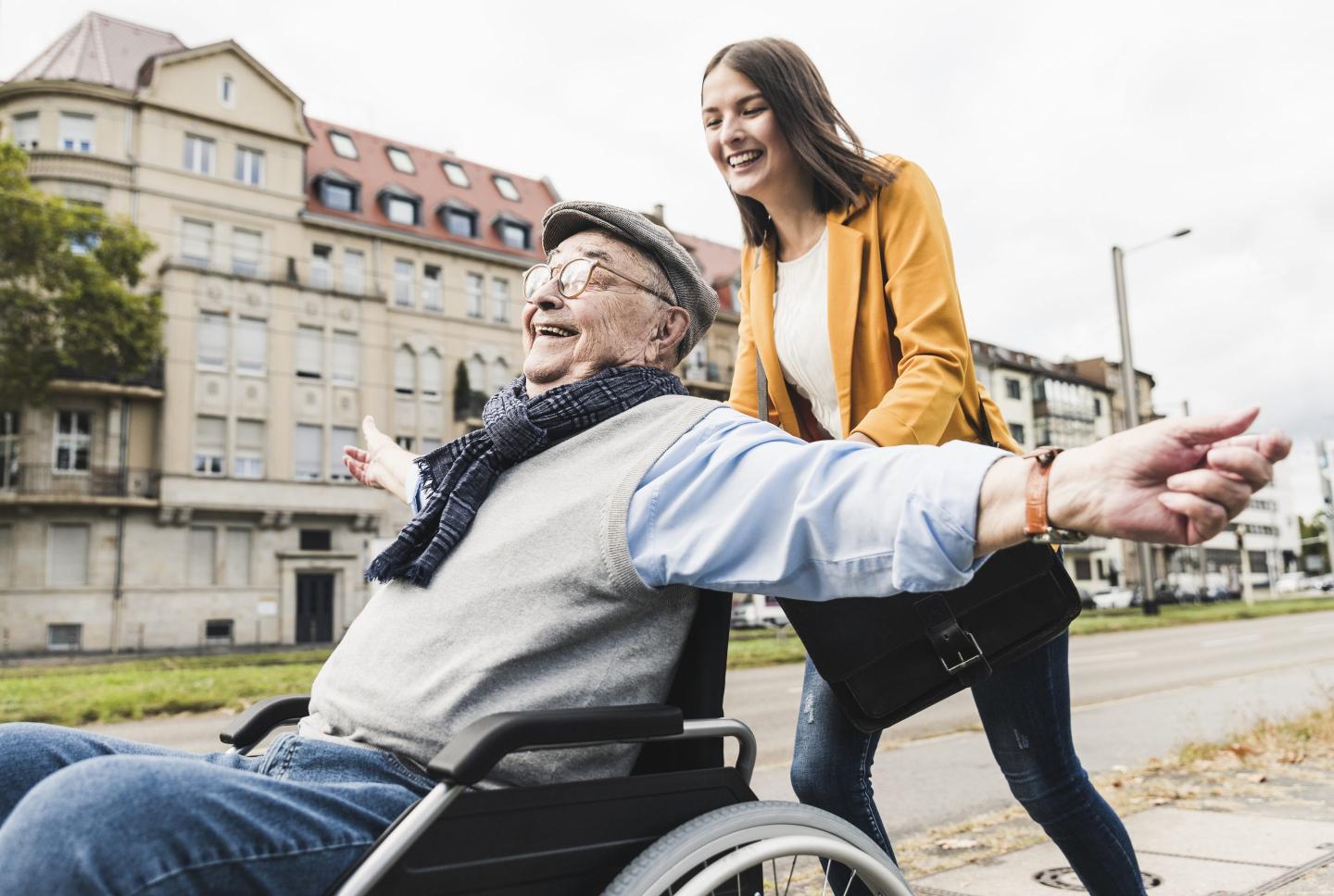 young woman pushing happy senior man in wheelchair