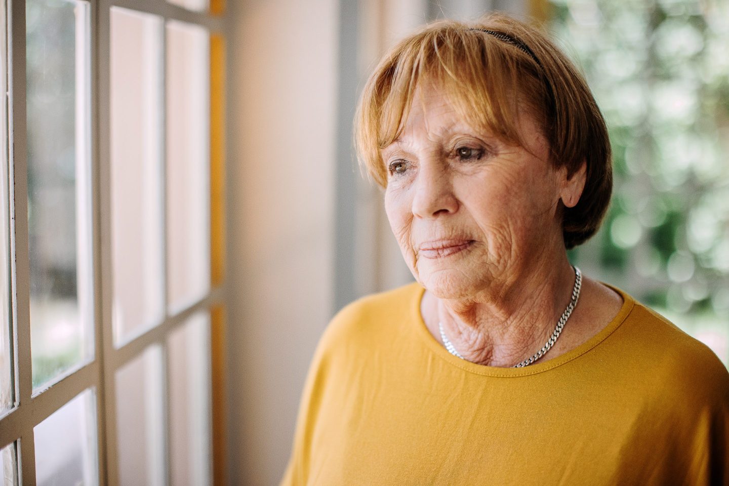 A retiree stares out the window looking sad