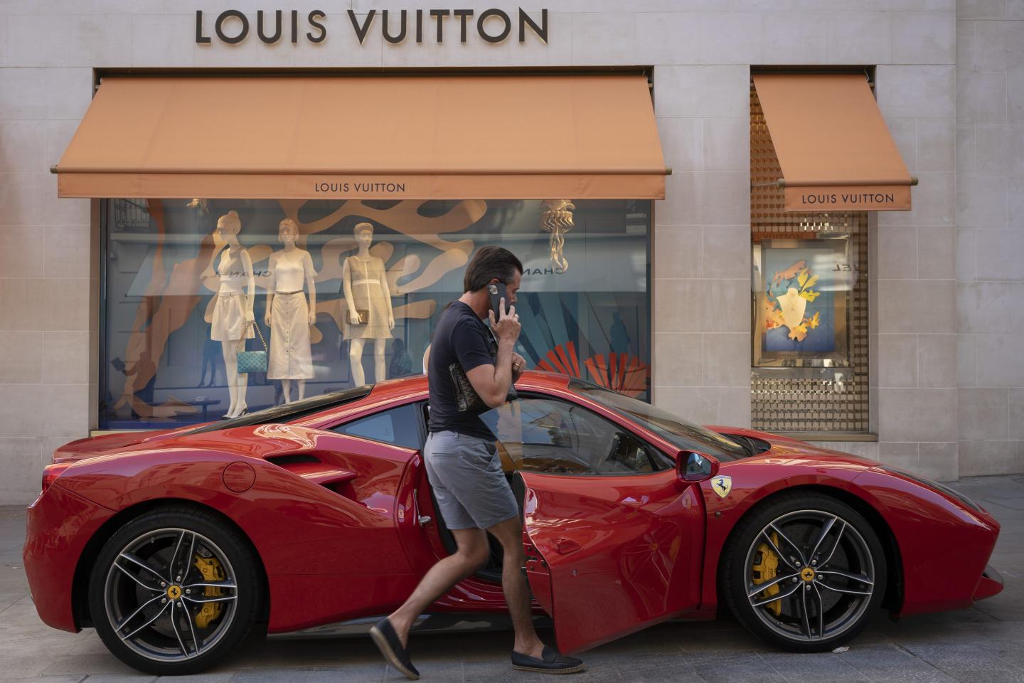 A driver returns to his red Ferrari parked on the pavement outside the Louis Vuitton store in Bond Street, on 12th August 2022, in London, England.