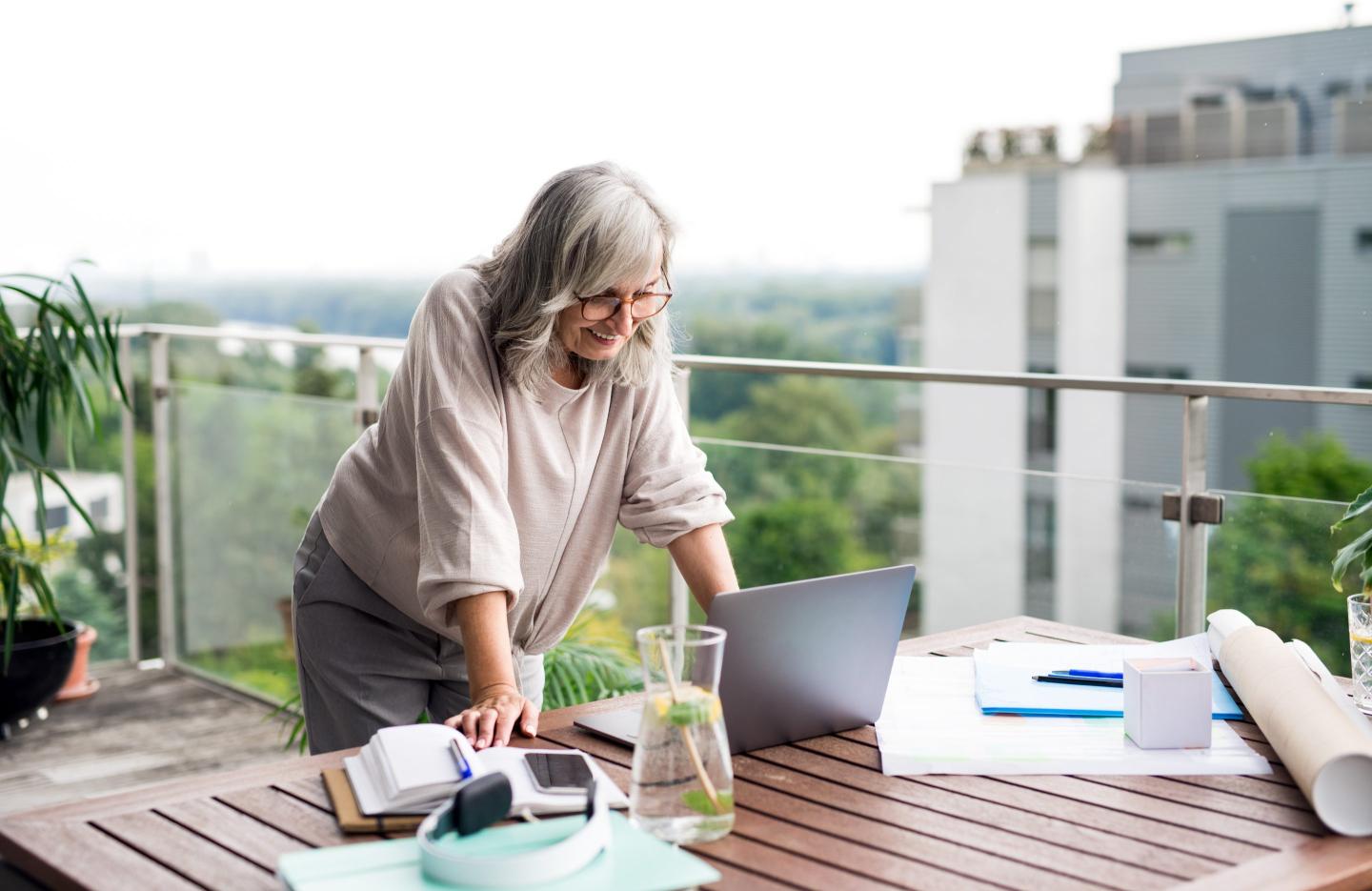 Active senior architect with laptop in home office, working outdoors on balcony.