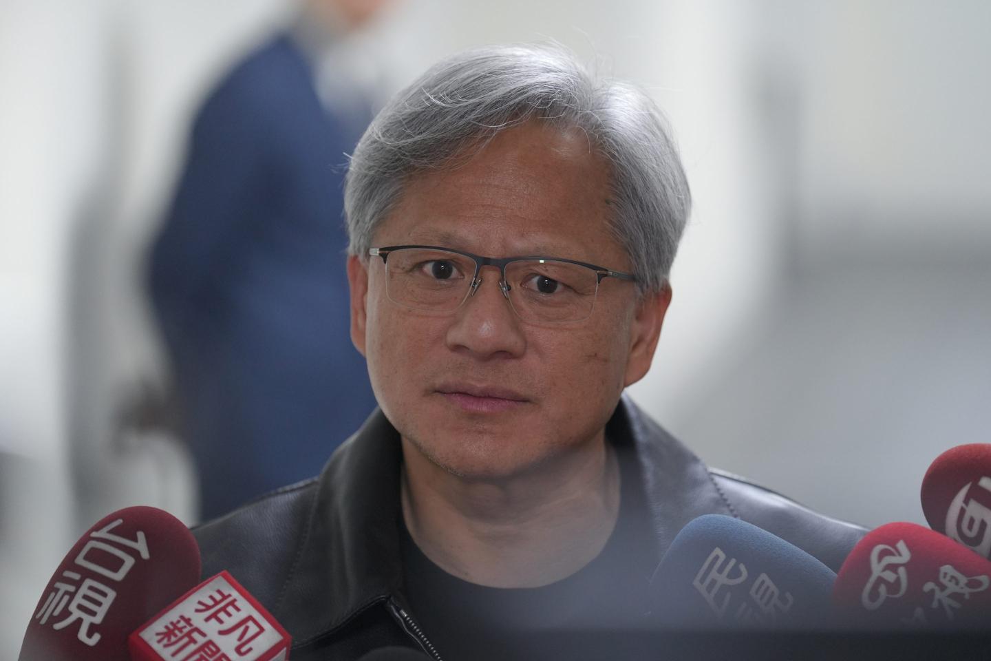Nvidia CEO Jensen Huang is standing behind a cluster of microphones with a concerned look on his face.
