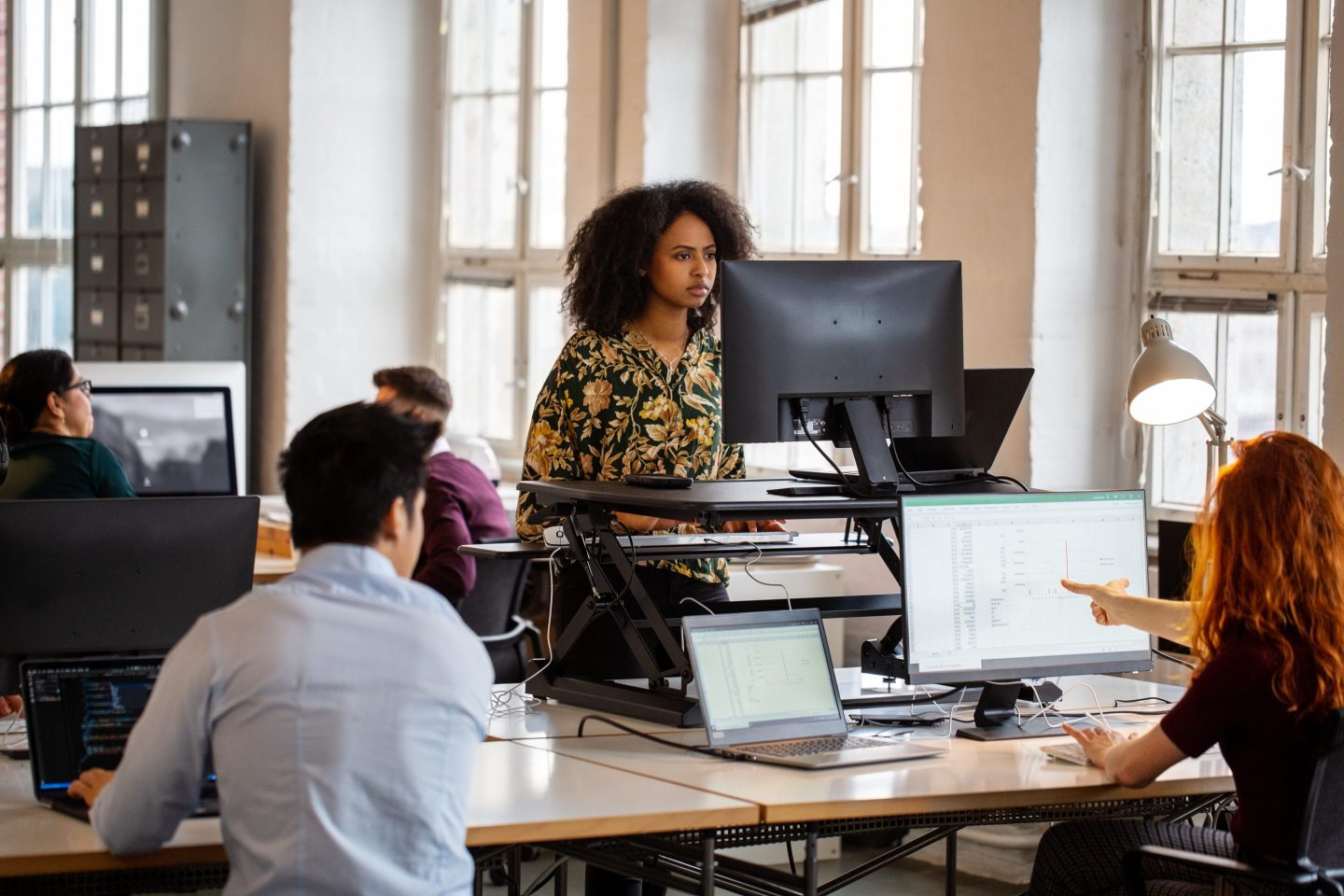 Young african woman working at a standing desk in office. Female employee working on computer at ergonomic standing desk.