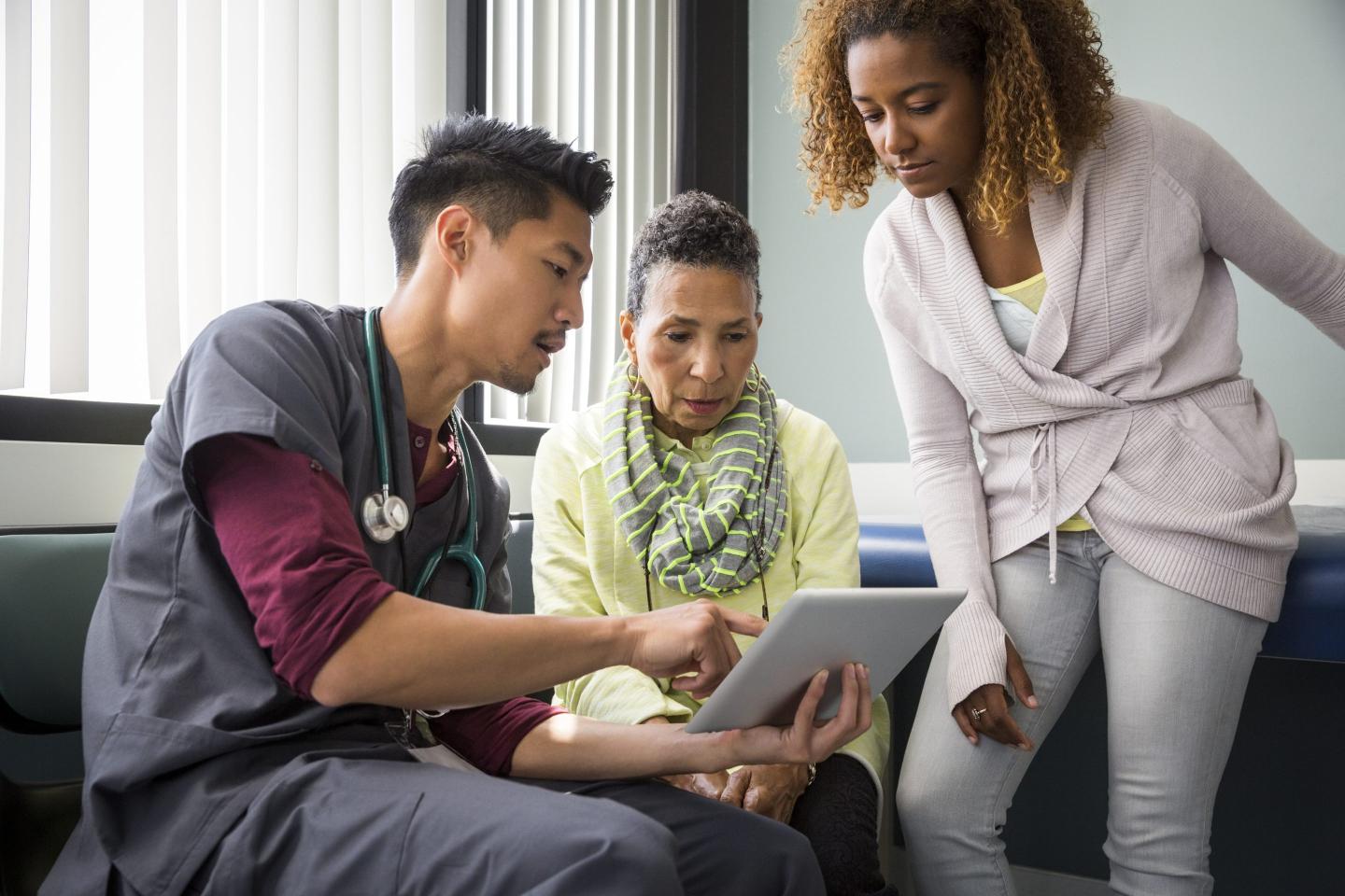Male nurse consulting with senior female patient and adult daughter in an exam room.