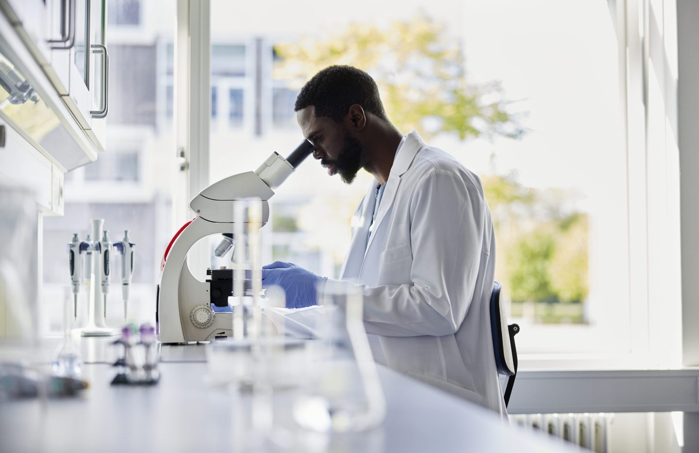 A scientist in a lab coat peers into a microscope in a lab.