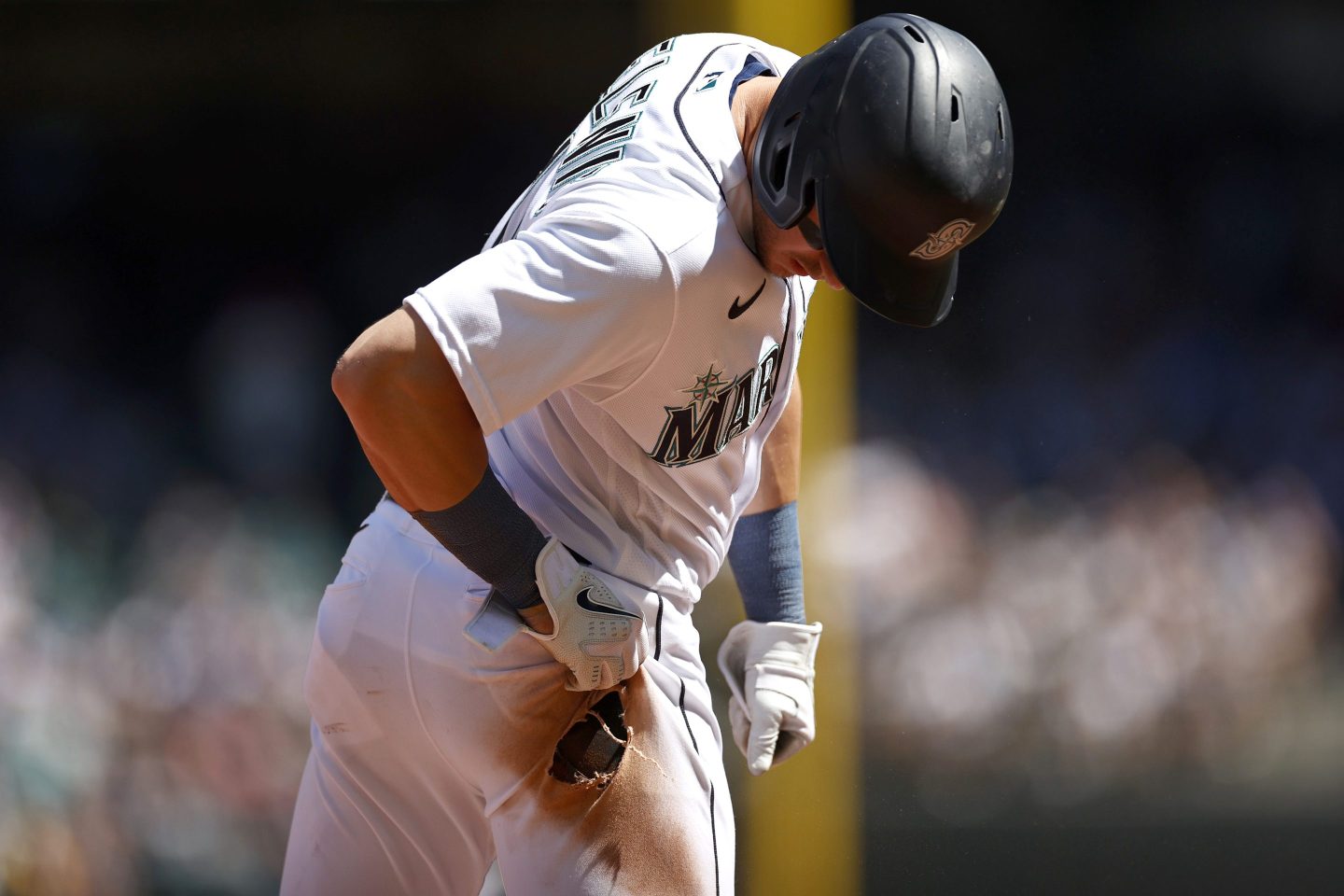 Jarred Kelenic is wearing a white baseball uniform and is looking down at a hole in his pants.