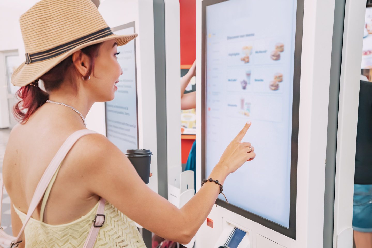 A woman is standing in front of a large screen with a food menu on it. She is selecting an item with her pointer finger.
