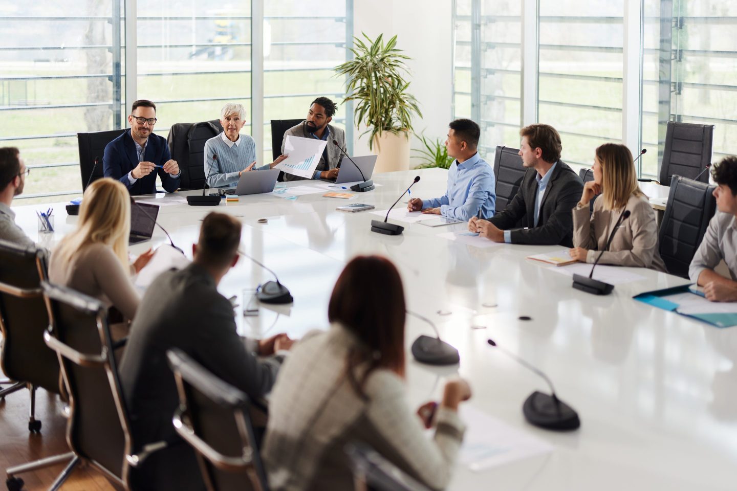 Group of business leaders having a meeting with large group of their colleagues at conference table. Senior woman is talking about reports.