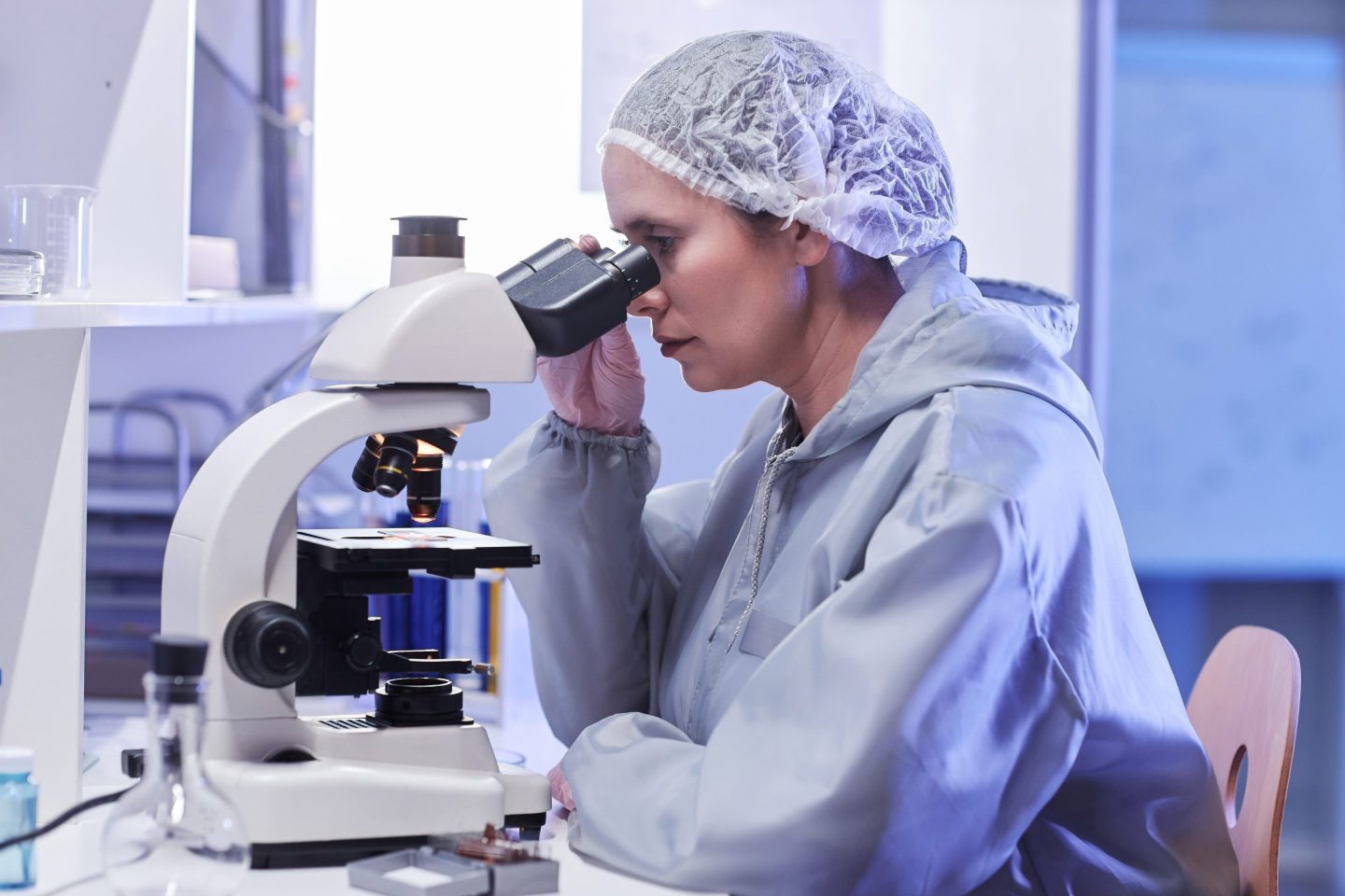 Side view portrait of female scientist looking in microscope in neon light while doing research in laboratory